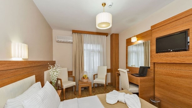 A hotel room with a bed, a desk with a laptop, a chair, a TV, and a window with curtains. - Selenay Hotel Istanbul (Istanbul)