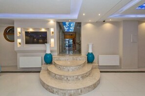 Eine geräumige Lobby mit einer Marmortreppe, einem großen Bildschirm und einem Blick zum Himmel durch eine Deckenöffnung.