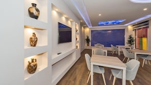 A modern interior with a flat-screen TV, shelves with decorative items, and a seating area with tables and chairs. - Selenay Hotel Istanbul (Istanbul)