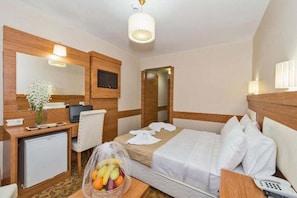 Ett hotellrum med en säng, ett skrivbord, en stol och ett litet kylskåp.