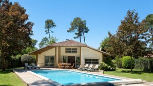 Ett hus med en swimmingpool, en uteplats med solstolar och en trädgård med träd.