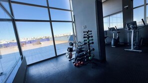 Un gimnasio con equipo de ejercicio y vistas de la ciudad a través de amplios ventanales.