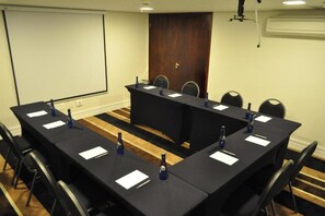A conference room with a long table, chairs, a projector screen, and an air conditioning unit. - Hotel Gran Vivenzo Belo Horizonte (Belo Horizonte)
