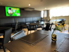 A restaurant with a modern interior, including a table with a vase of flowers and a screen displaying an advertisement. - Hotel Gran Vivenzo Belo Horizonte (Belo Horizonte)