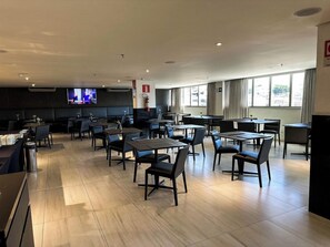 A spacious restaurant with multiple tables and chairs, a television screen, and large windows. - Hotel Gran Vivenzo Belo Horizonte (Belo Horizonte)