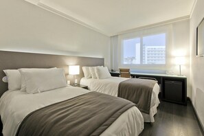A hotel room with two beds, a desk, a chair, a lamp, and a view of a building through the window. - Hotel Gran Vivenzo Belo Horizonte (Belo Horizonte)