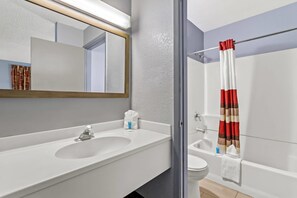 A bathroom with a white sink, mirror, and shower curtain. - Rodeway Inn Albuquerque NM (Albuquerque)