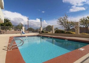 A swimming pool with a metal ladder, surrounded by a fence, and a clear sky above. - Rodeway Inn Albuquerque NM (Albuquerque)