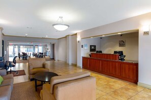 Un hall de hotel con mostrador de recepción, zona de estar y vista al comedor.