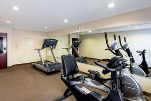 Un gimnasio equipado con cintas de correr, bicicletas estáticas y un espejo grande.