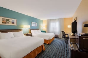 Een hotelkamer met twee bedden, een bureau met een computer, een televisie en een raam met gordijnen.