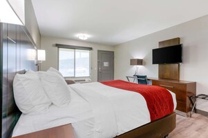 A hotel room with a bed, a desk, a television, and a window.