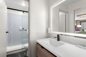 Ein modernes Badezimmer mit einer einbruchsicheren Dusche, einem weißen Waschbecken und einem großen Spiegel.