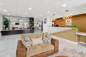 Ein Hotel-Empfangsbereich mit einer Rezeption, einer Wartezone inklusive Sofa und Kissen sowie einem modernen Interieur.