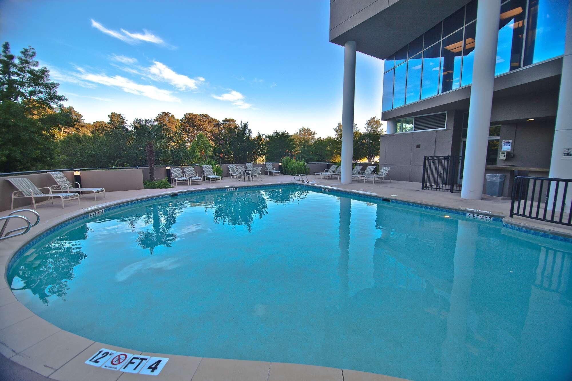 A swimming pool with lounge chairs, a poolside area, and a building with large windows.