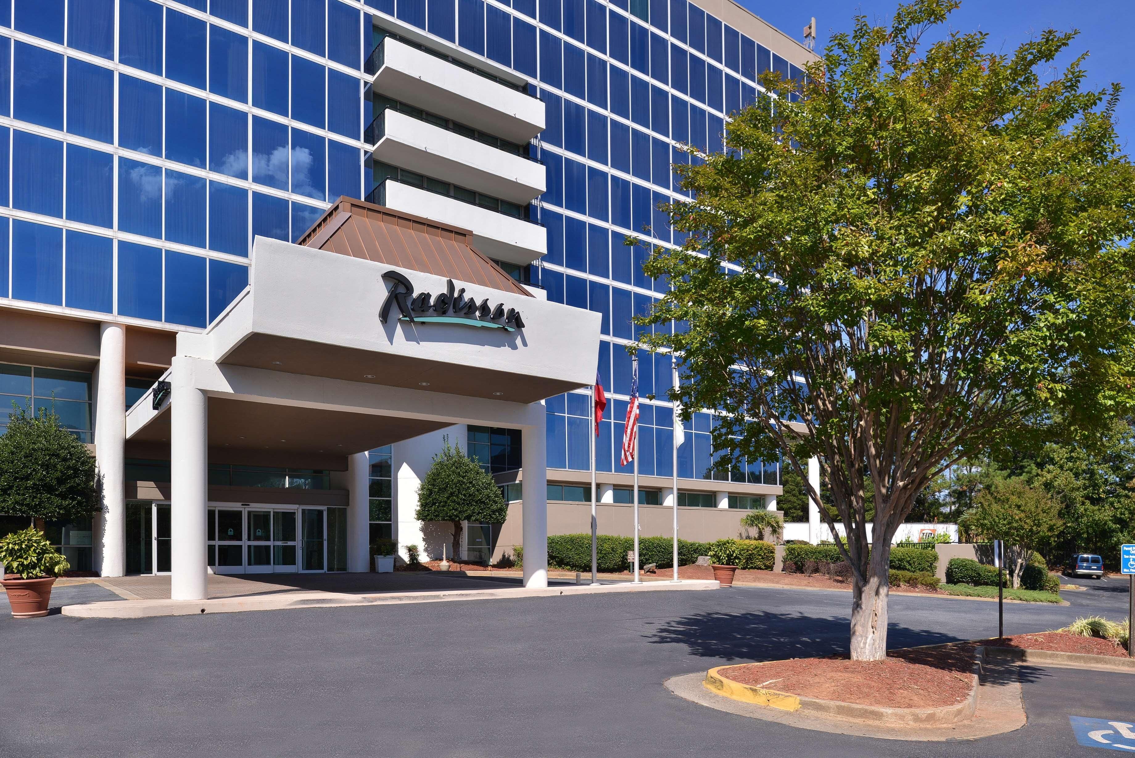 A modern building with a glass facade, a prominent entrance with a sign, and a tree in the foreground.