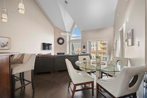 Un salon moderne avec une table à manger en verre, un canapé et un téléviseur fixé au mur.