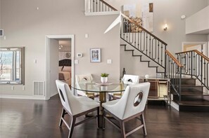 A spacious living area with a glass dining table, white chairs, a staircase, and a view of a bedroom. - Lakeview Townhouse in Sunset Waterfront Resort (Kelowna)