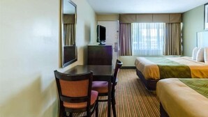 A hotel room with a bed, a desk with a chair, a television, and a window with curtains. - Econo Lodge (Pittsfield)