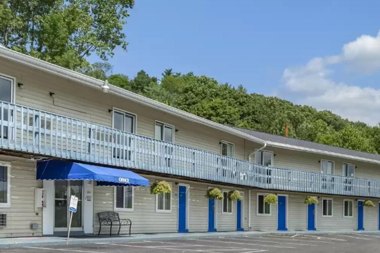 A motel with a row of rooms, a blue awning, and a balcony with railings.