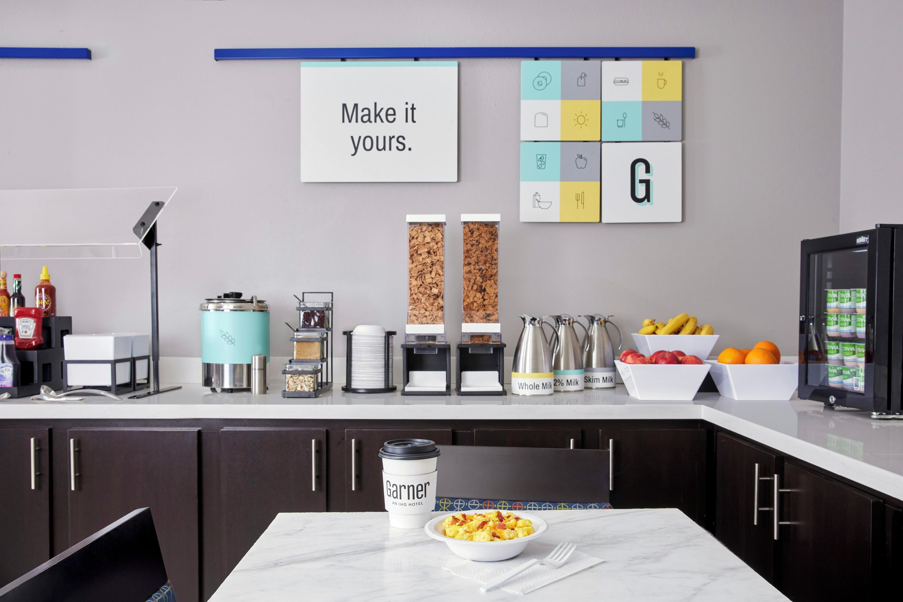 A modern kitchen with a coffee maker, a bowl of cereal, and a sign that says 'Make it yours.'