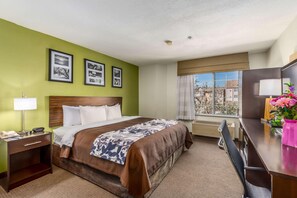 Habitación de hotel con una cama grande, un escritorio, una silla, una lámpara y una ventana con vistas a edificios.