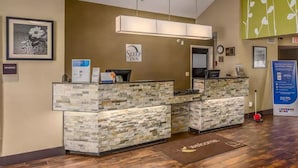 A reception desk with a stone facade, a clock, and a 'Welcome' mat. - Rodeway Inn Airport Albuquerque, NM (Albuquerque)