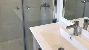 Un baño con cabina de ducha de vidrio, un lavabo blanco con grifo cromado y un espejo.
