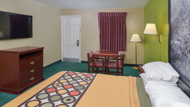 A hotel room with a bed, a desk with chairs, a dresser, a television, a door, and a wall with a lamp. - Super 8 Little Rock North Airport (North Little Rock)