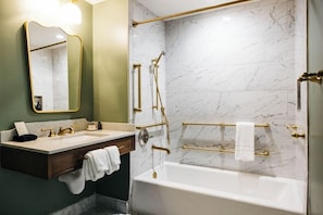 Ein Badezimmer mit Marmorwand, einer weißen Badewanne, einem Waschtisch mit Spiegel und goldenen Armaturen.