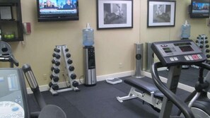 A gym with treadmills, dumbbells, a water dispenser, and a TV displaying news. - Artmore Hotel (Atlanta)