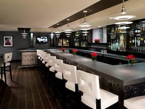 Eine Bar mit einer langen Theke, weißen Barhocker und Deckenleuchten.