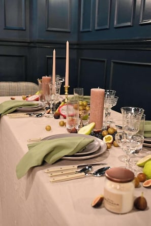 Una mesa servida con velas, platos, cubiertos y frutas.