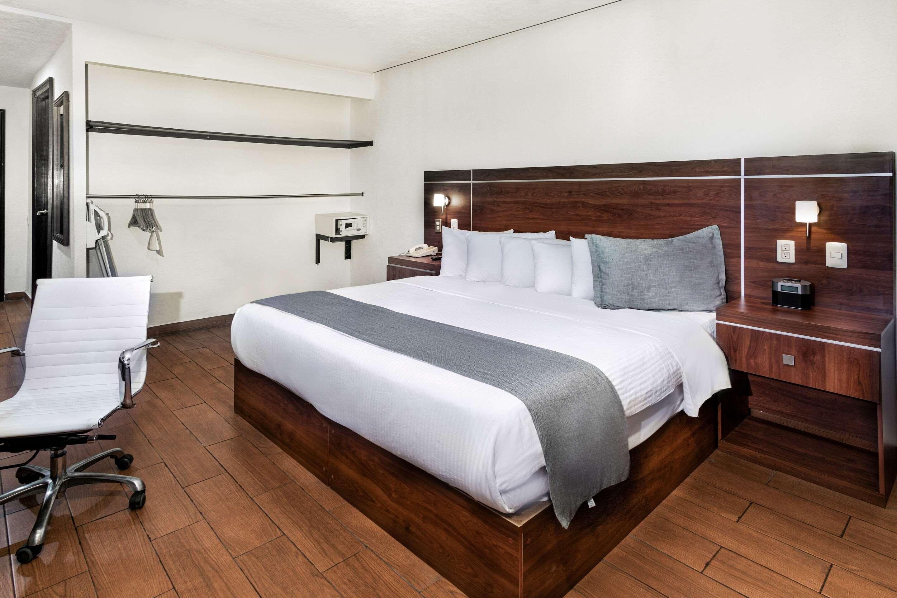 Una habitación de hotel con una cama grande, un escritorio, una silla y una mesita de noche con lámpara.