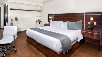 Una habitación de hotel con una cama grande, un escritorio, una silla y una mesita de noche con lámpara.