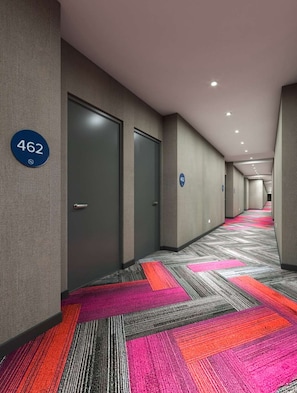 A hotel corridor with a carpeted floor, doors, and a number sign. - Tru by Hilton Saltillo (Saltillo)