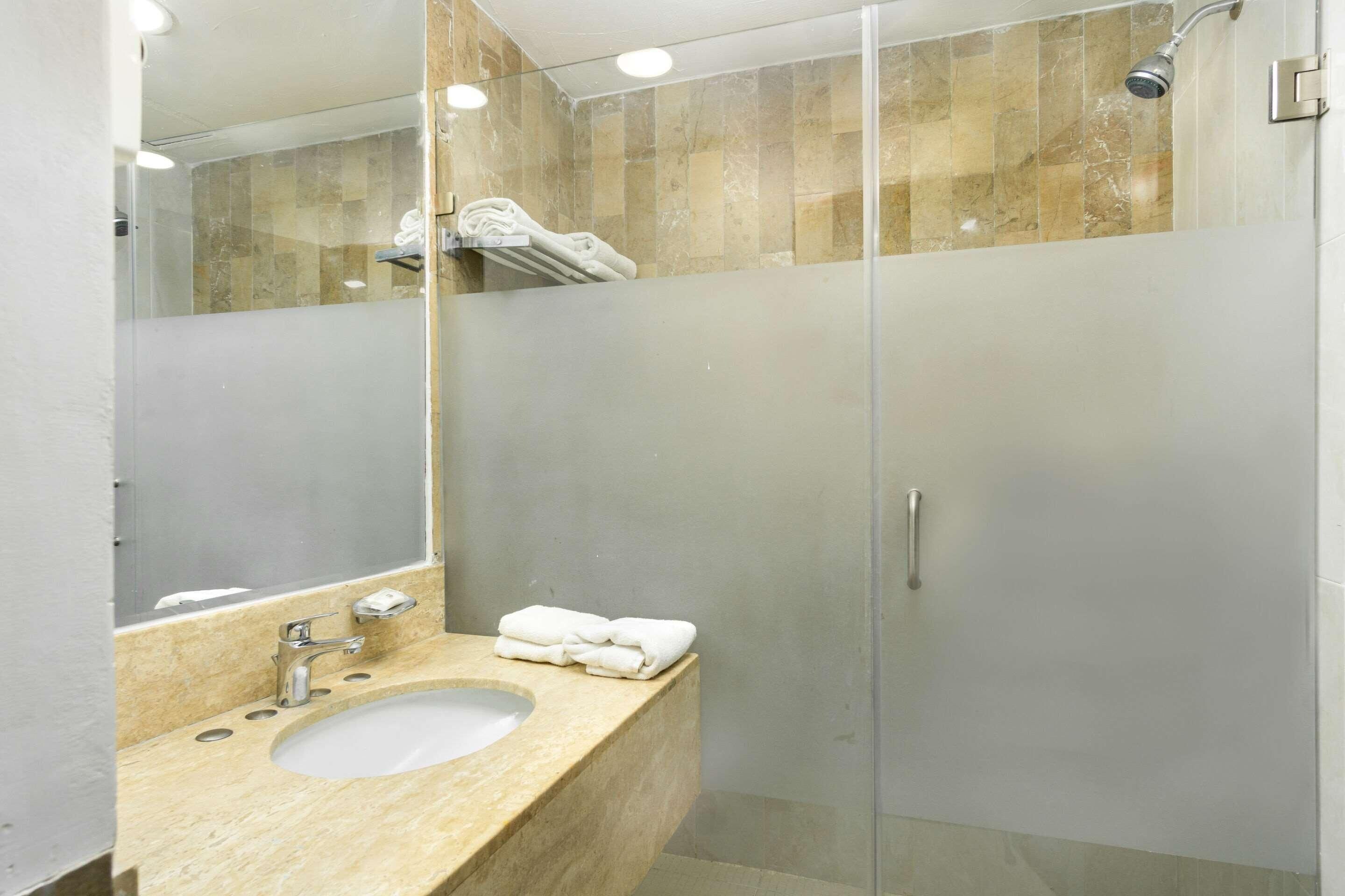 Un baño moderno con ducha envuelta en vidrio, un lavabo con encimera de mármol y un espejo grande.