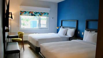 Habitación de hotel con dos camas, un escritorio, una silla y ventana con vista a edificios.