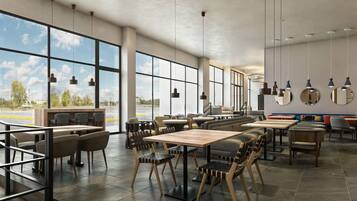 A spacious indoor area with large windows, multiple seating arrangements, and hanging pendant lights.