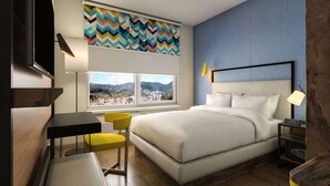 A hotel room with a bed, a desk, a chair, a nightstand, a lamp, and a window with a view. - Tru by Hilton Saltillo (Saltillo)