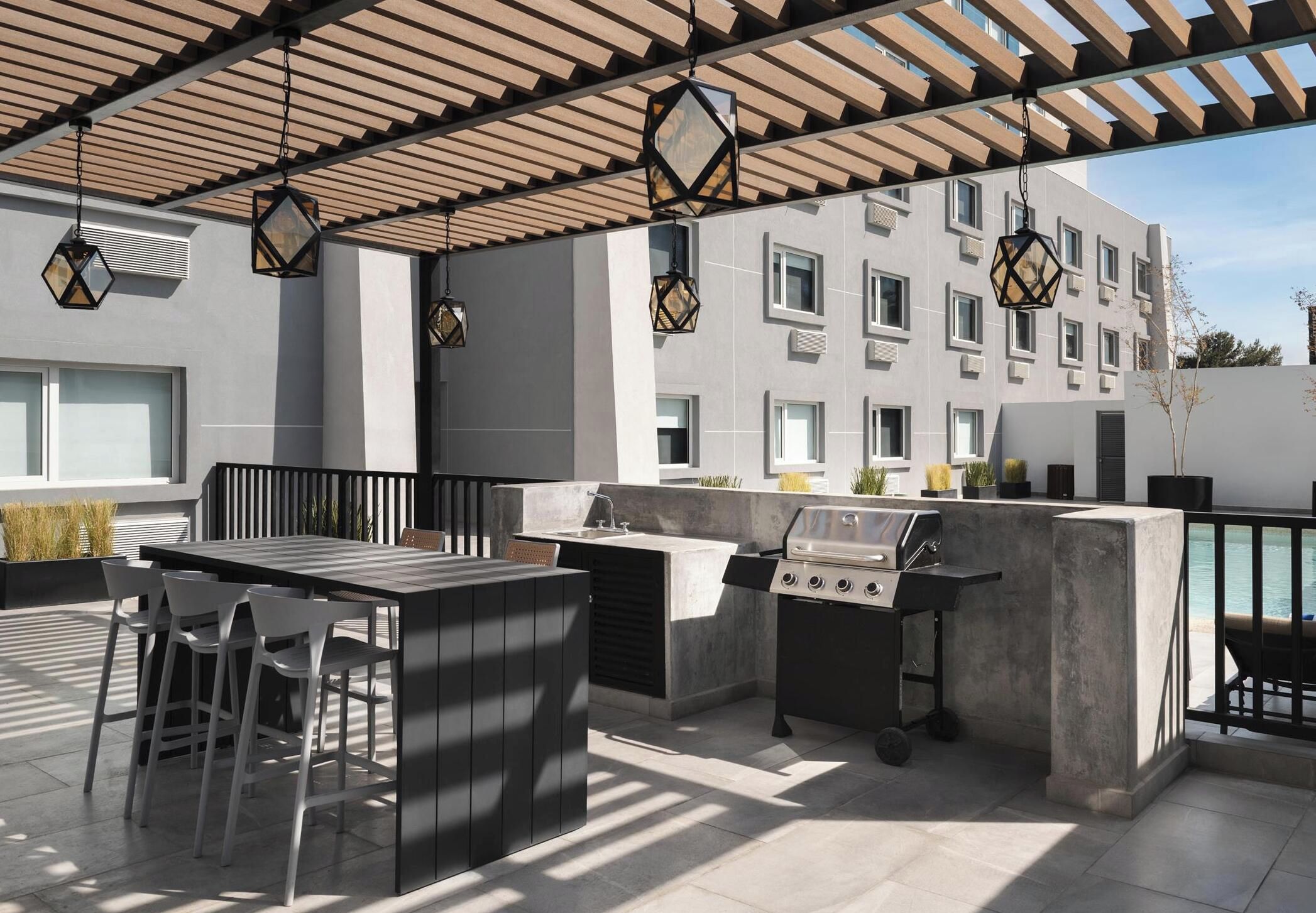 An outdoor patio with a grill, seating, and a pergola with hanging lanterns.