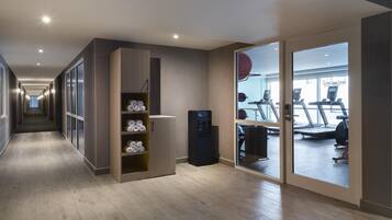 Un pasillo moderno de hotel con un gimnasio visible a través de una puerta de vidrio.