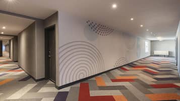 Un pasillo de hotel con alfombra estampada, una puerta y un muro con diseños circulares.