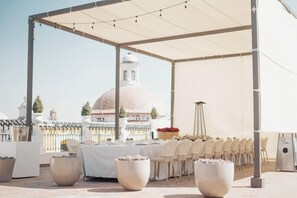 An outdoor dining area with a covered pergola, tables set for a meal, and a view of a dome-shaped building in the background. - Palacio San Leonardo (Puebla)