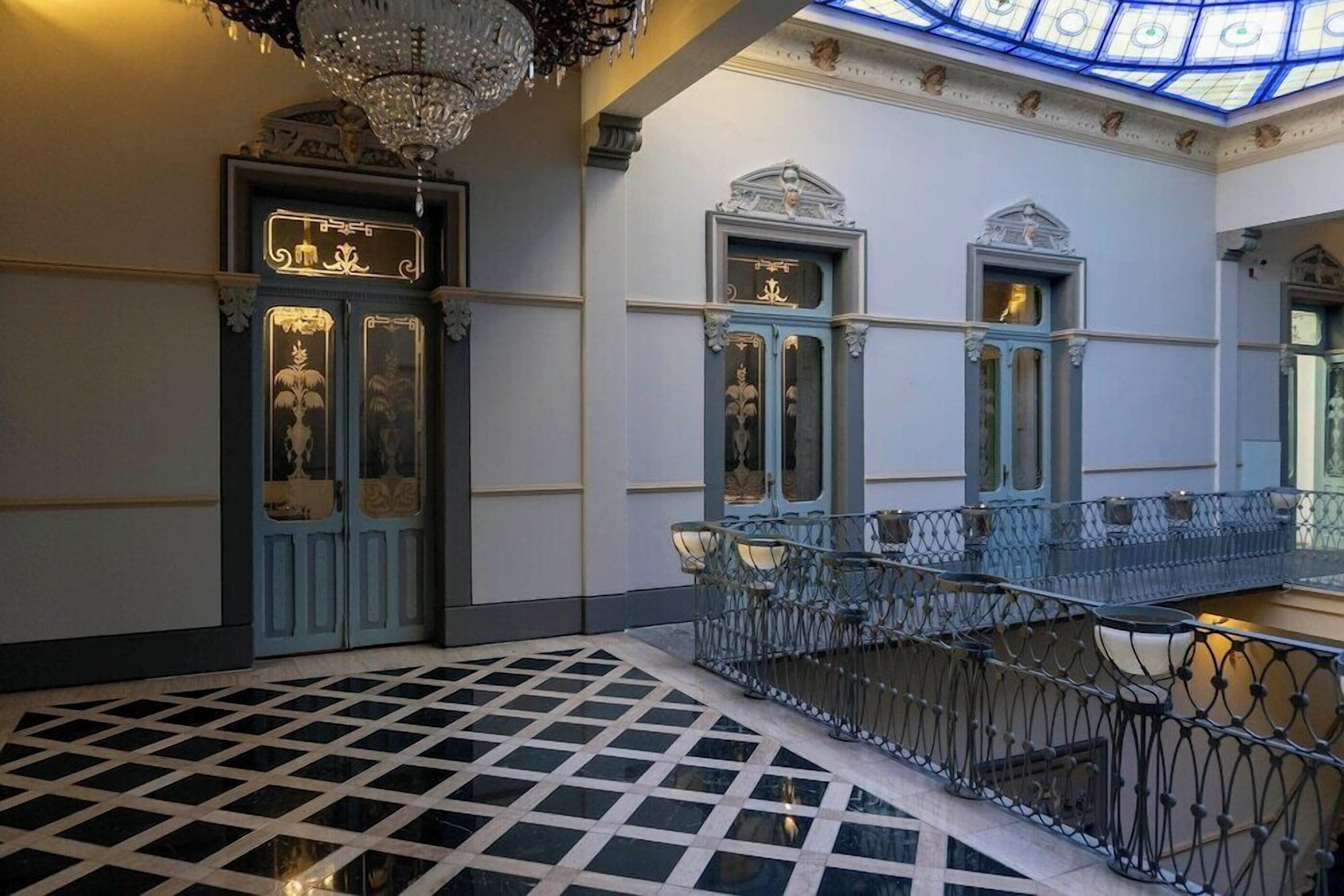 A grand interior with ornate doors, a glass ceiling, and a patterned floor.
