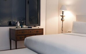 A hotel room with a bed, a nightstand with a lamp, a dresser, and a window with a view of the city at night. - Palacio San Leonardo (Puebla)