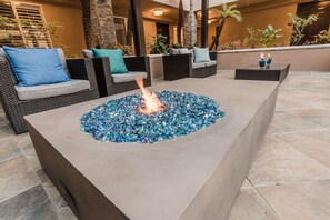 A fire pit with blue glass tiles, surrounded by wicker furniture and a stone planter. - Manhattan Beach Hotel (Manhattan Beach)