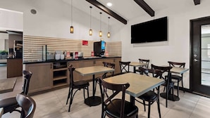 A modern restaurant interior with a bar area, multiple tables and chairs, pendant lighting, and a flat-screen TV mounted on the wall. - Manhattan Beach Hotel (Manhattan Beach)