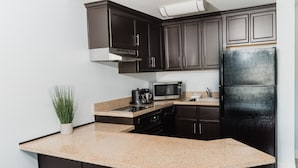A kitchen with dark cabinets, a black refrigerator, a microwave, and a granite countertop. - Manhattan Beach Hotel (Manhattan Beach)