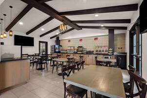Um restaurante moderno com vigas de madeira aparentes, uma área de bar central e uma televisão de tela plana na parede.